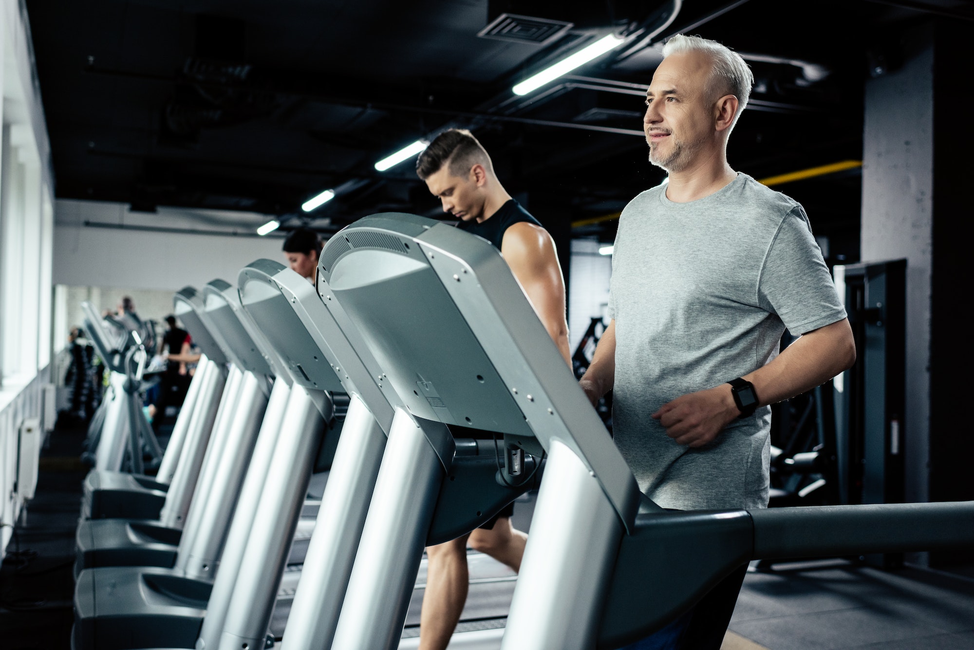 senior and young sportsmen running on treadmills in sport center